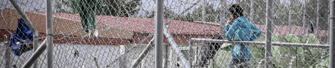Jeune homme derrière les grilles d'un camp de détention en Grèce