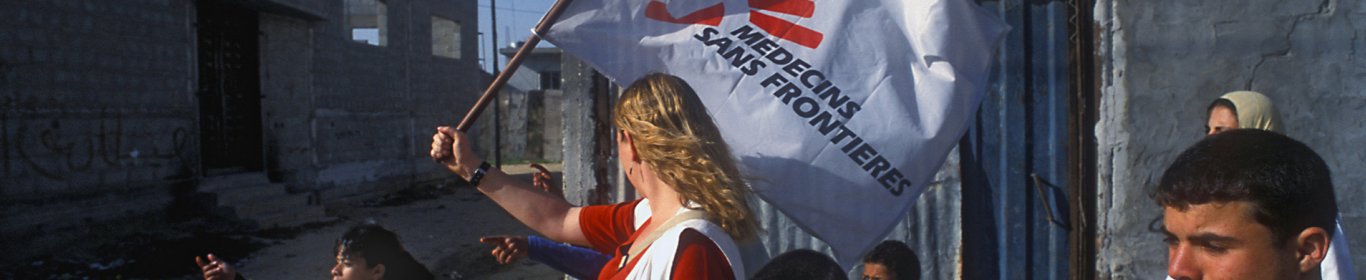 Une coordinatrice entourée d'enfants avance avec un drapeau MSF pour éviter les tirs