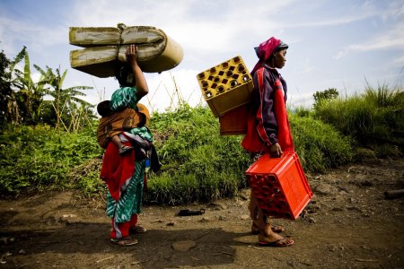 Deux femmes transportent un matelas et des affaires sur une route