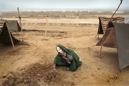 Une femme fait le ménage autour d'un abris construit avec des tissus et du bois