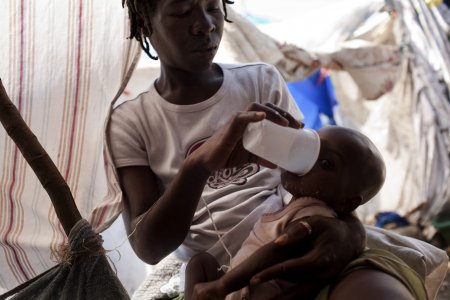 Une femme aide un enfant à boire dans un camp de Port-au-Prince en Haiti