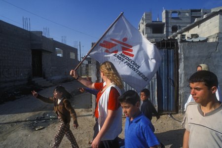 Une coordinatrice entourée d'enfants avance avec un drapeau MSF pour éviter les tirs